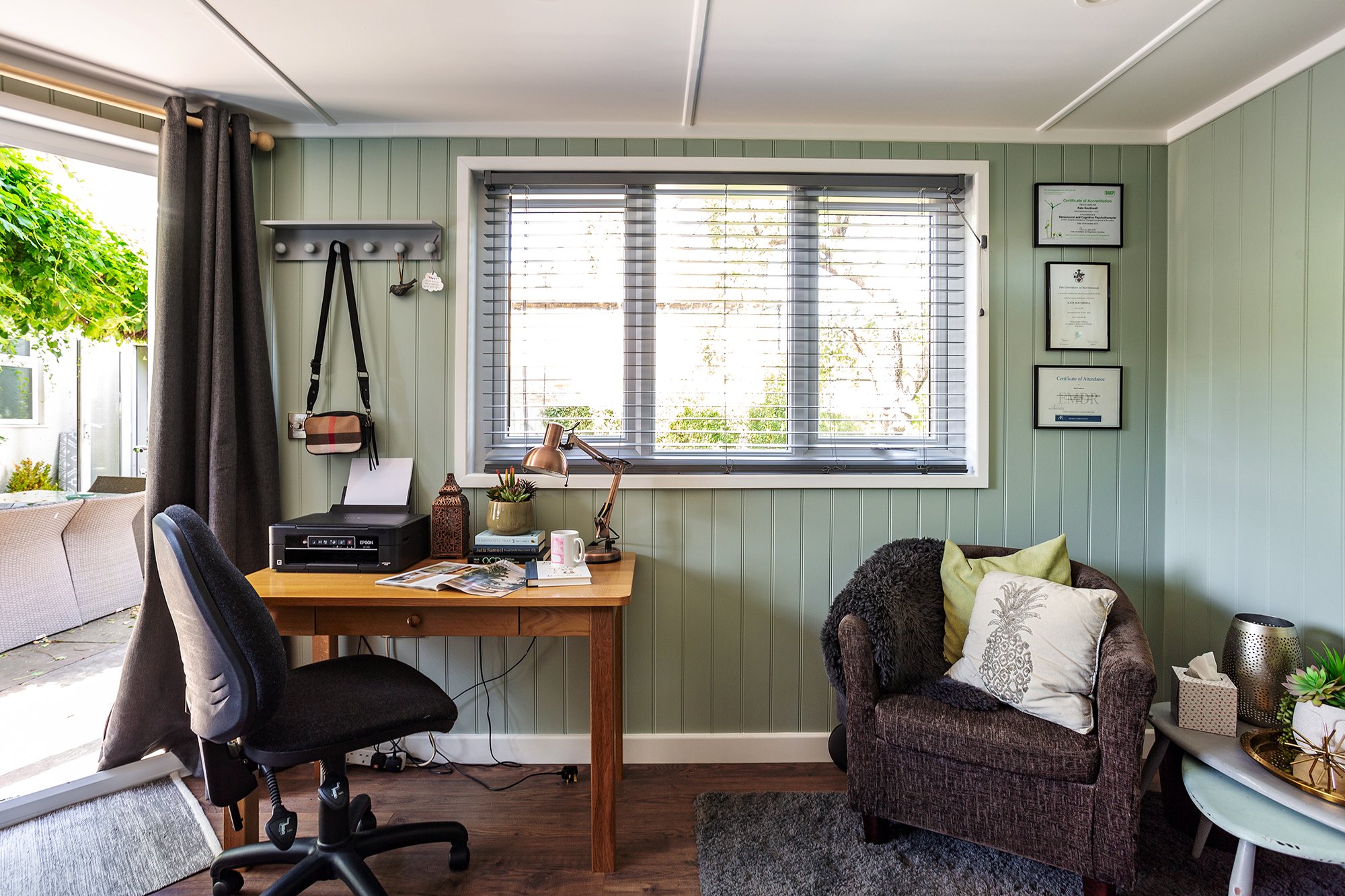 Insulated Garden office with sage green walls, desk, chair and comfy seating