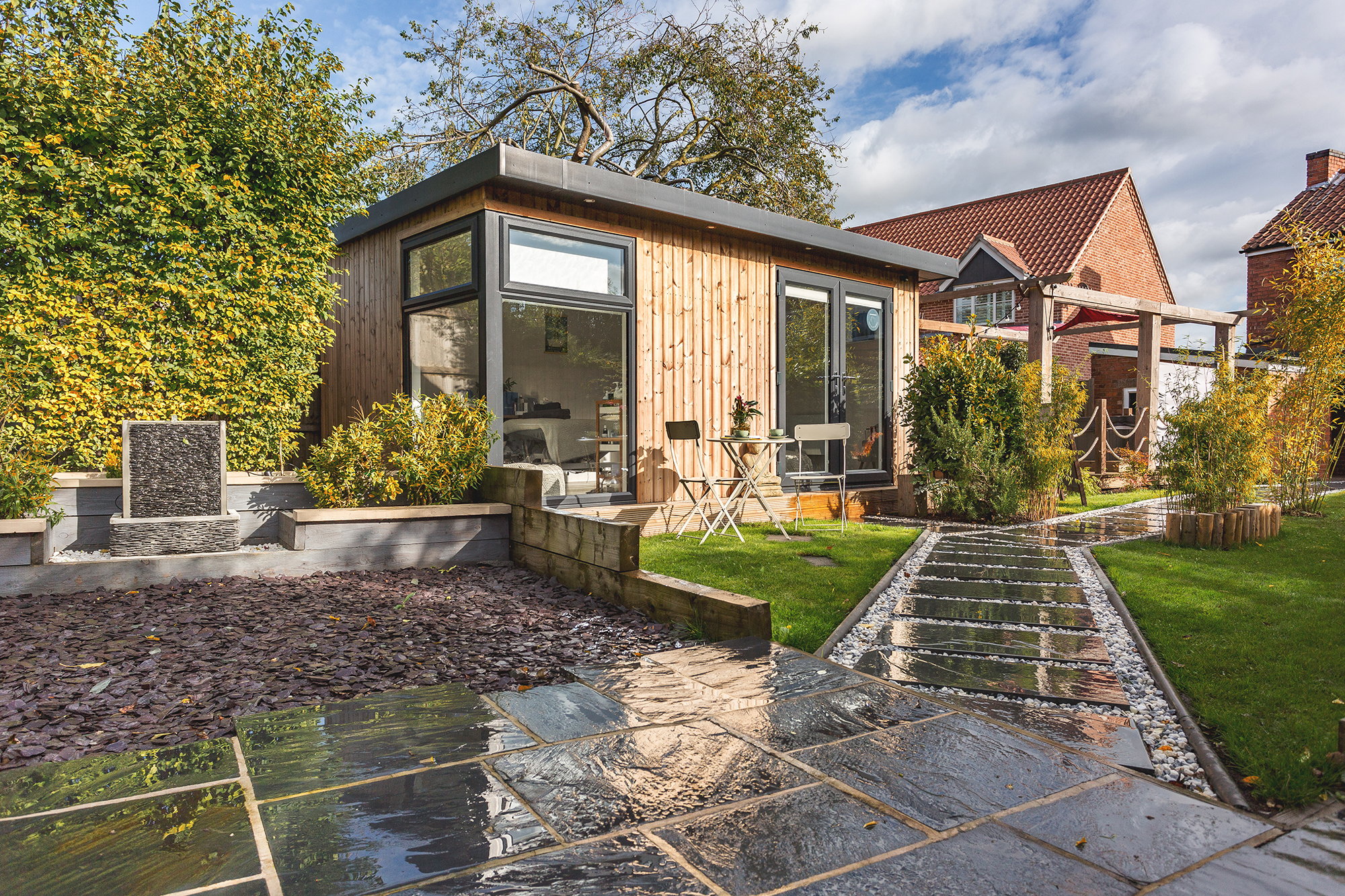 Insulated timber garden room with black french doors and nice neat pathway leading up to room