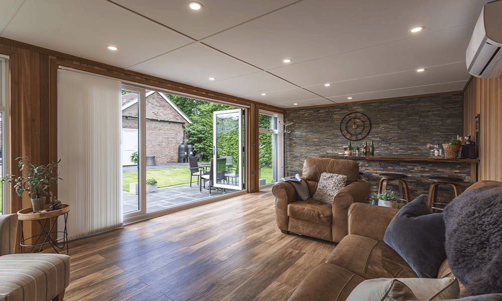 large garden bar building with open bifold doors and leather sofas inside it, with views of lawn area and garden furniture