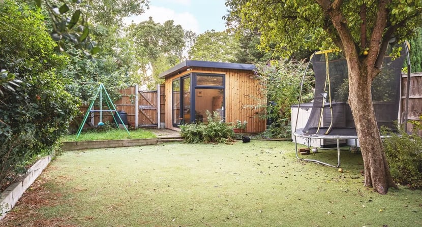 Wooden garden room set in a family-friendly backyard with a swing set and trampoline—offering a peaceful, separate space for children or teens to focus on homework and revision away from household distractions