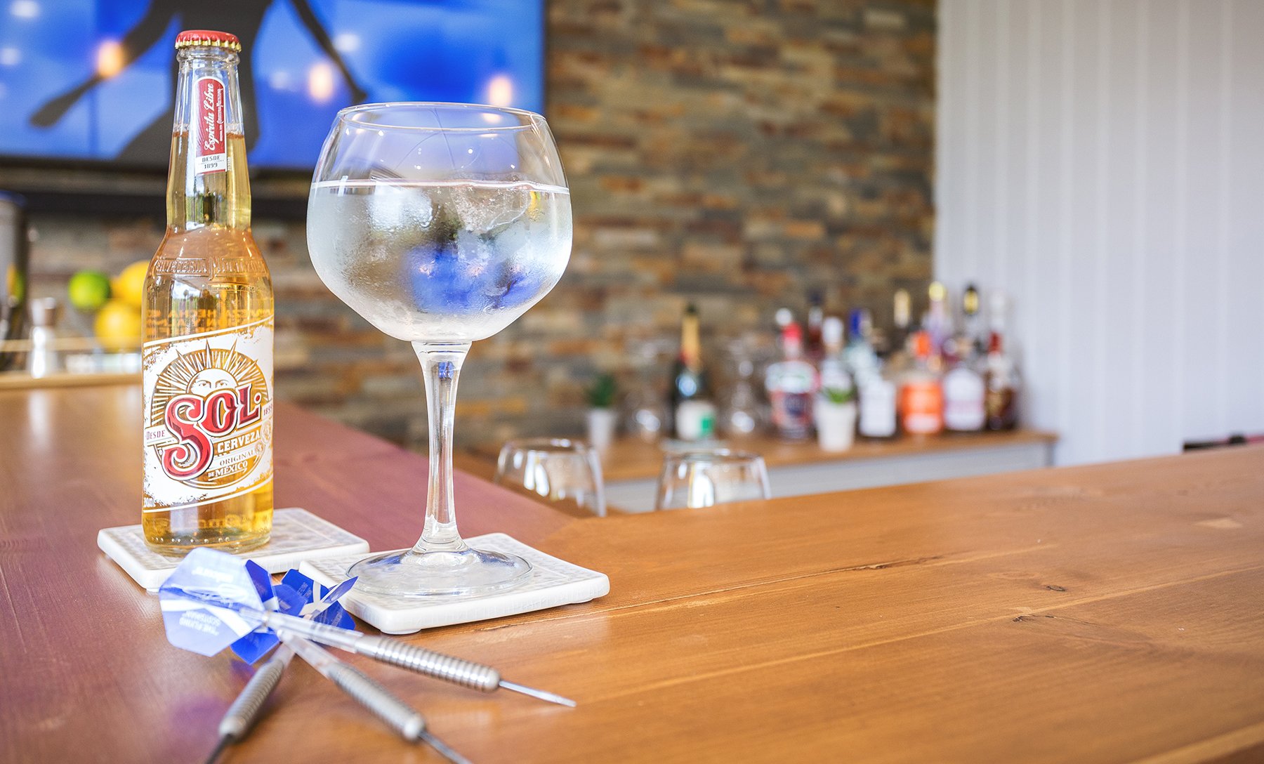 Close up of gin a tonic glass on bar with darts, inside a garden bar