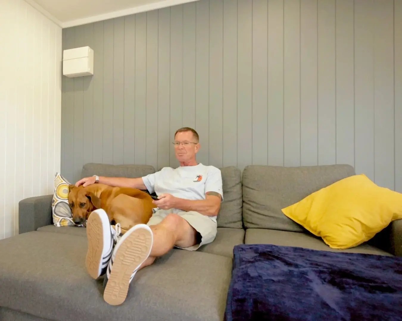Parent relaxing with the family dog on a grey sofa inside the garden room.