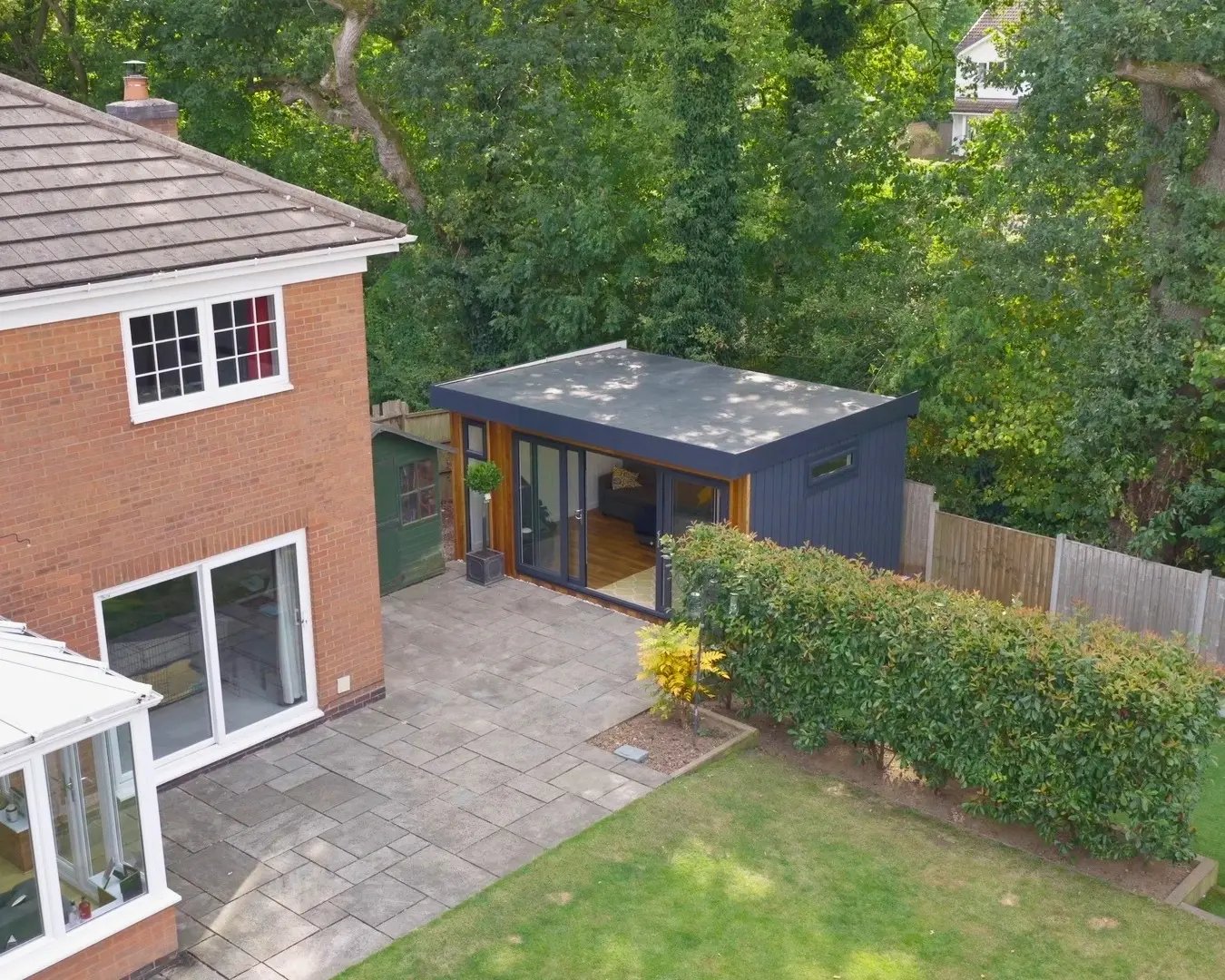 Aerial view of a modern cedar-clad garden room beside a family home and patio.