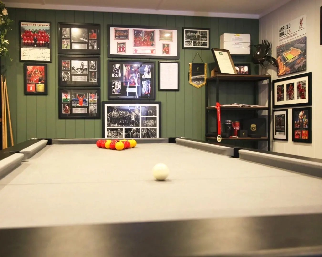 Close-up of a pool table inside a garden games room, with framed sports memorabilia covering the feature wall behind.