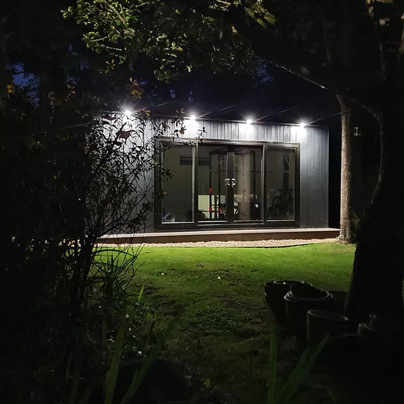 garden gym marley board with spot lights and roof overhang in garden area with squat rack and bench press and exercise equipment