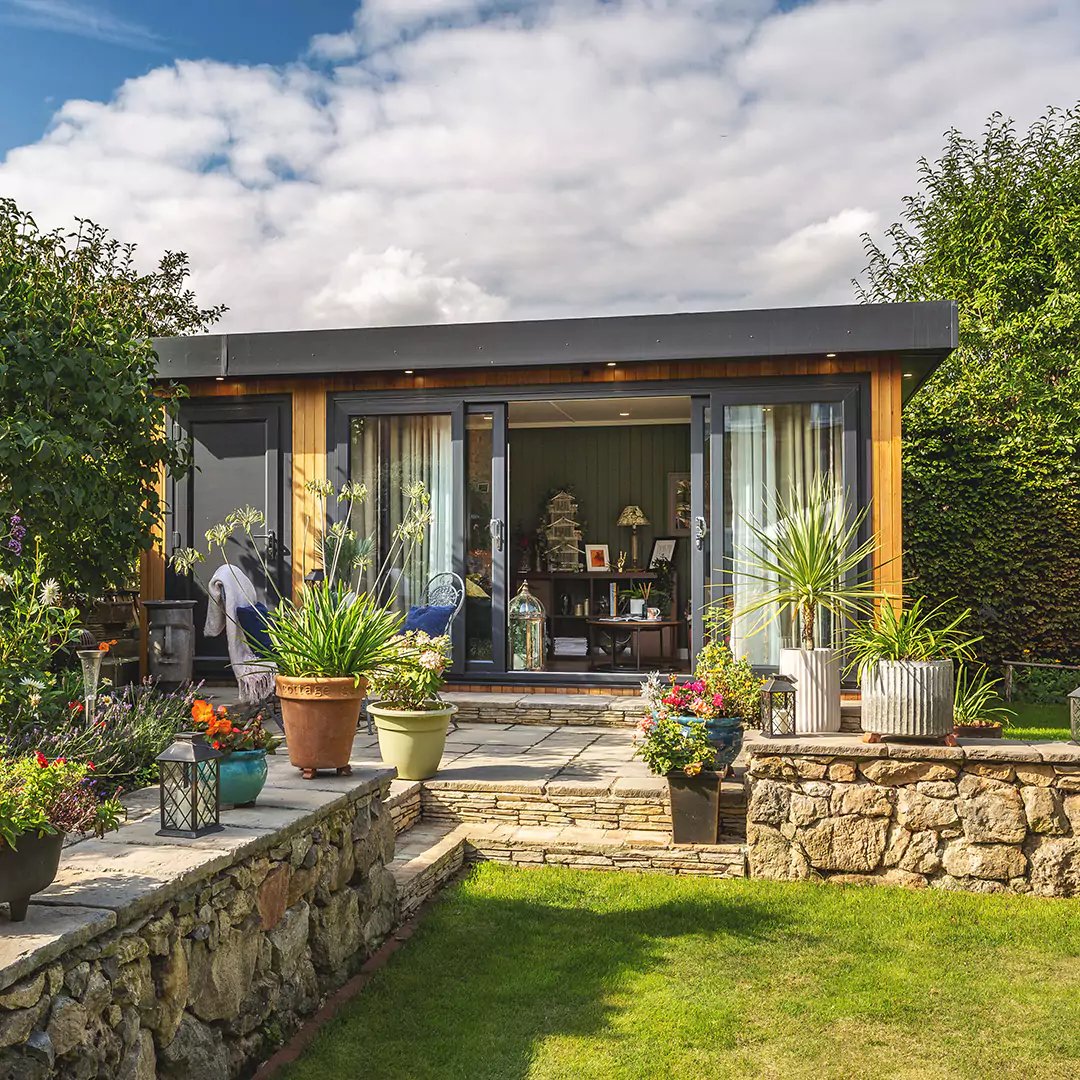 cedar garden office pod with lawn area and patio decking with potted plants 