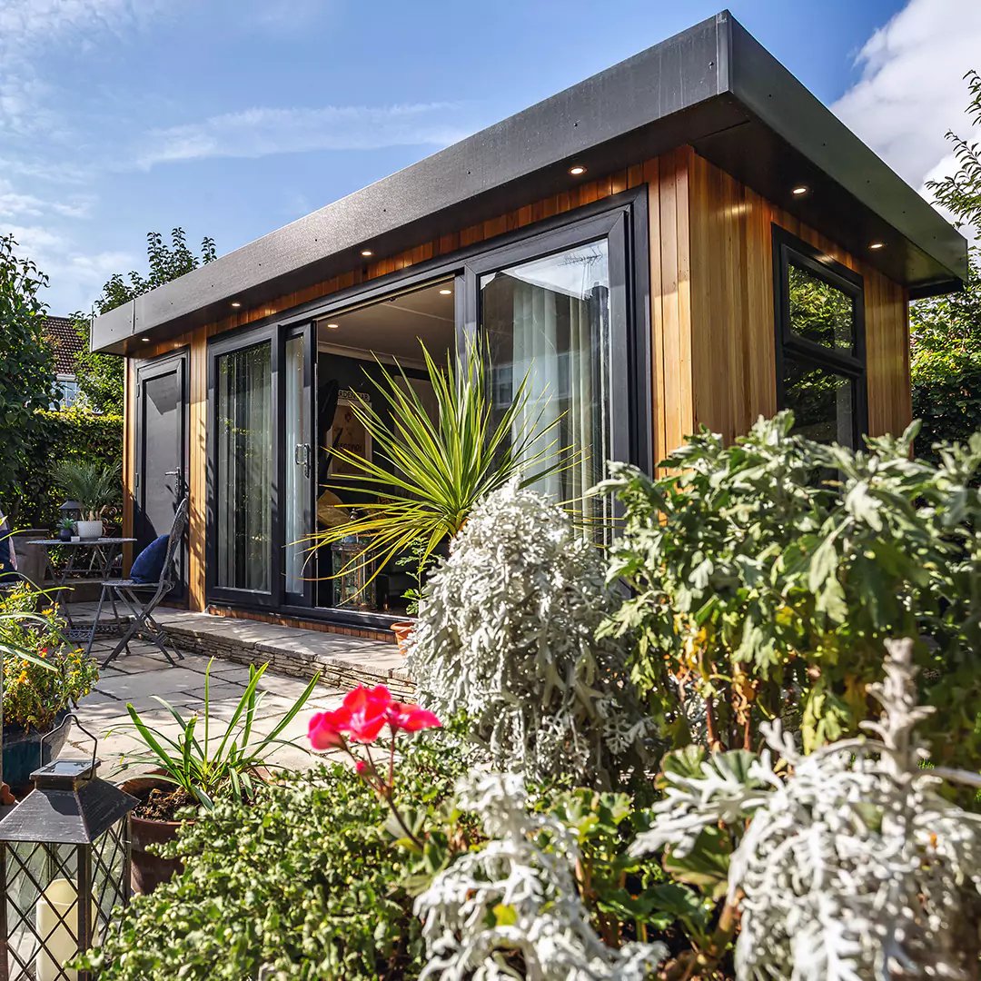 cedar garden office pod with lawn area and patio decking with potted plants 