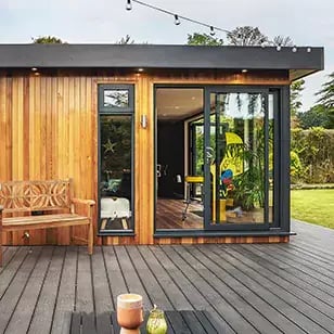 A timber deck with a large garden man cave and a bench and table on it