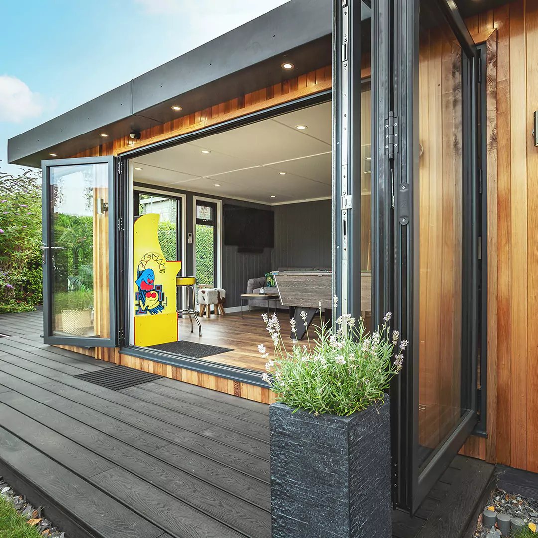 a large garden man cave room with a vintage arcade game and wooden deck and open bifold doors