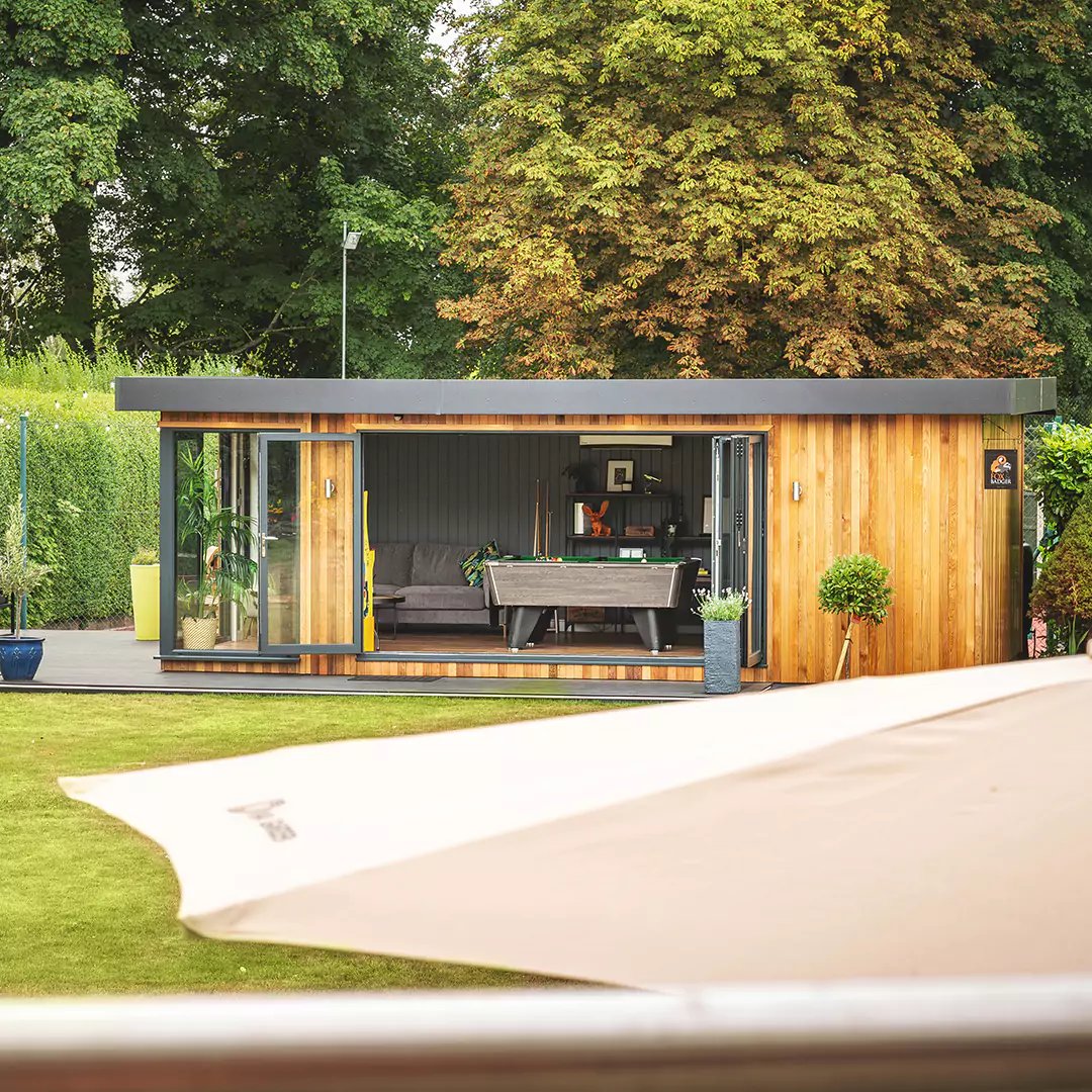 large cedar garden room with open bifold doors and large green lawn area with timber step