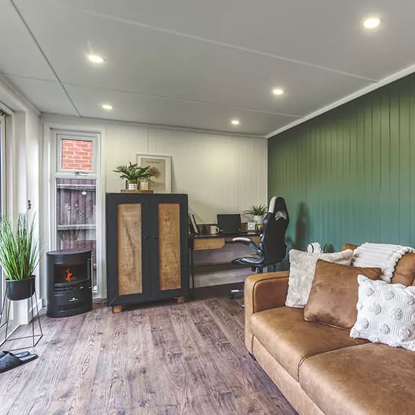 Interior of a garden office pod lounge with rust coloured sofa & green plants for decor