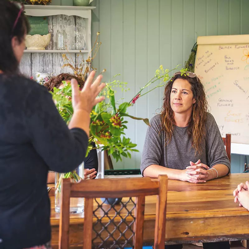 women gathered around a table inside a large home business garden room partaking in a floristry workshop