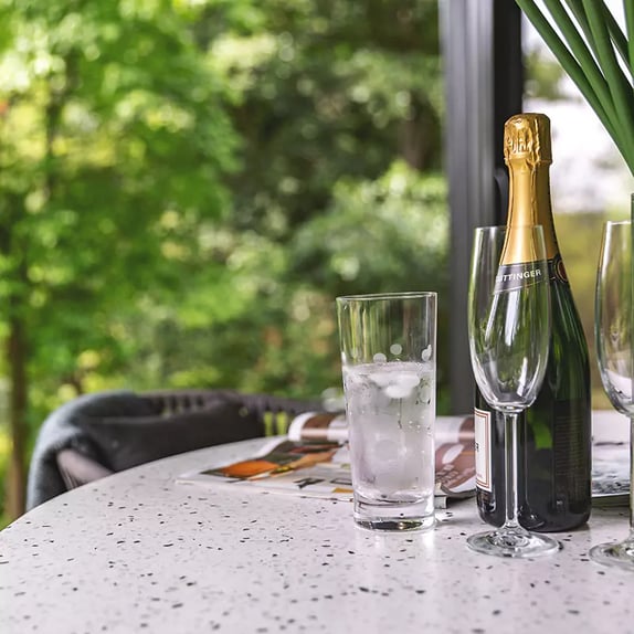 Exterior shot of a garden room with canopy close up shot of bistro table with bottle of champagne, glasses, open magazines and flowers in vase