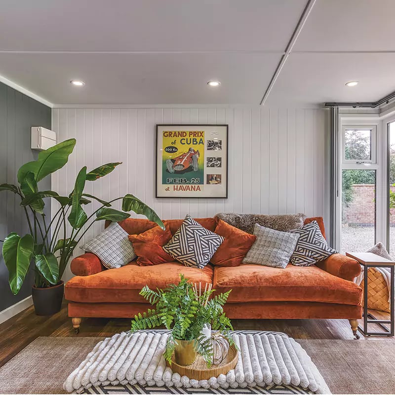 Interior of a garden office pod lounge with rust coloured sofa & green plants for decor