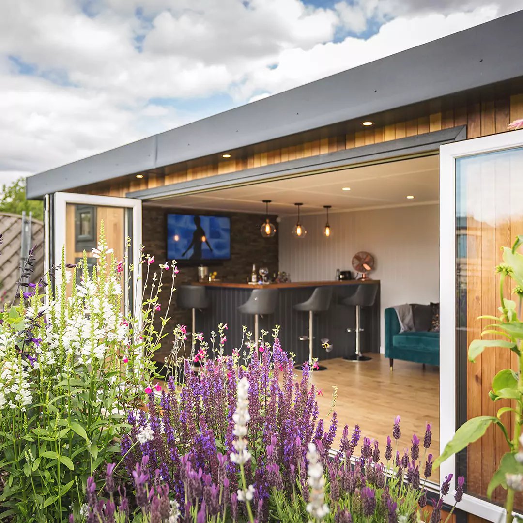 Cabin Master Cedar Garden Building with rattan outside furniture and bright bean bags with patio area and grassy lawn in foreground with view of swim spa and large buddha wall art