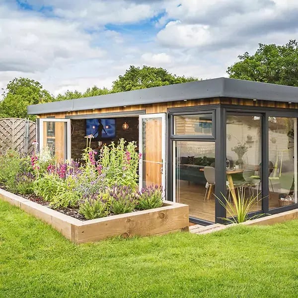 large garden man cave building with open bifold doors and with plant bed and lawn area in front