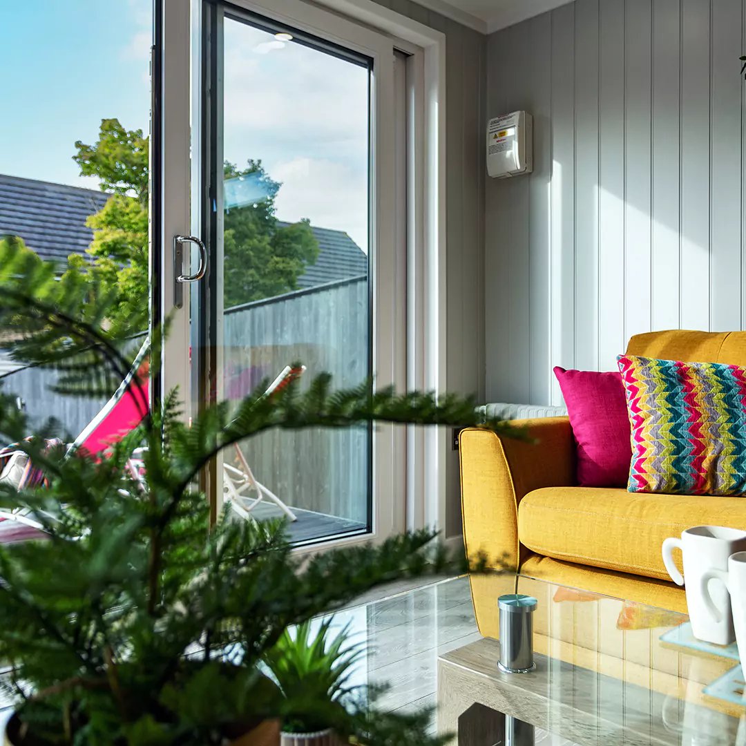Inside an insulated garden studio with yellow sofa and bright pink cushions with plant