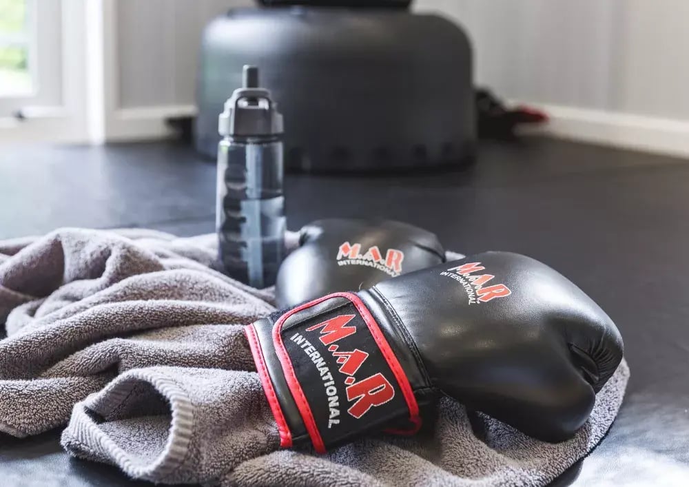 close up of boxing gloves and water bottle on floor inside garden gym
