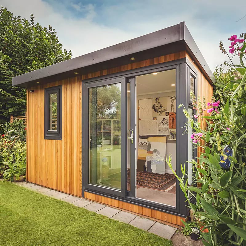cedar garden room artists studio with green trellises and garden furniture and flowers and hedges