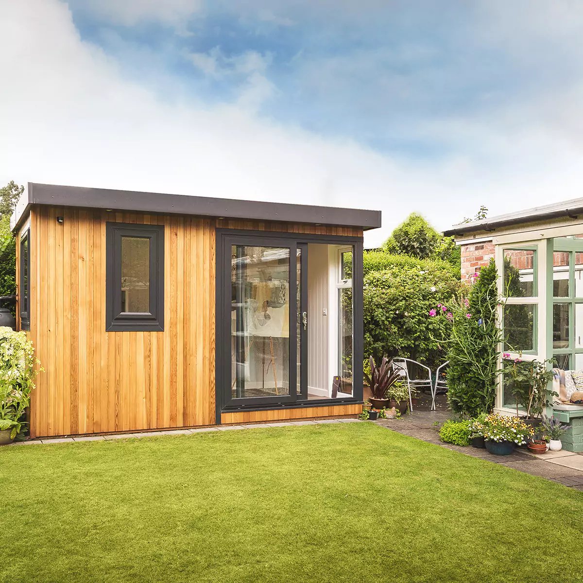 External shot of a cedar garden office next to sage green conservatory