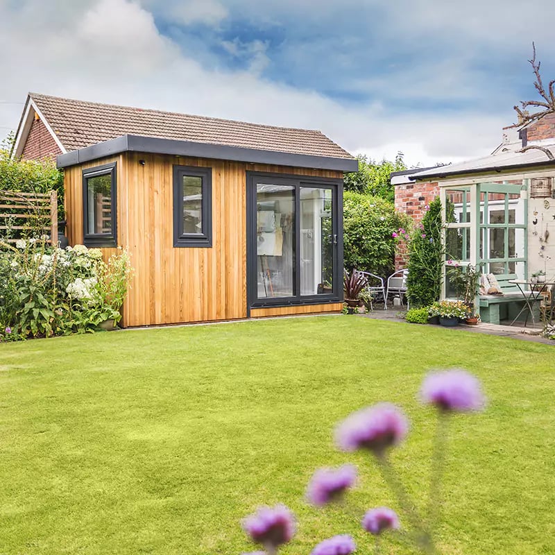 cedar garden room artists studio in patio area with grass and hedges and flower beds