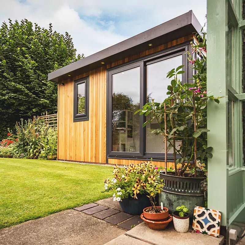cedar garden room artists studio with green trellises and garden furniture and flowers and hedges