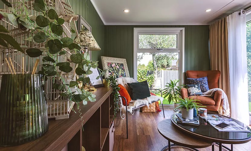 Interior of a cosy garden room snug with dark green walls and green velvet sofa