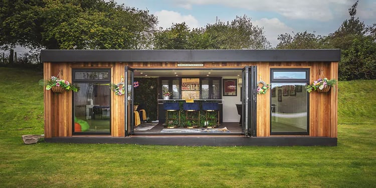 Looking inside a luxury garden bar with bifold doors open so you can see bar seating and bright decor