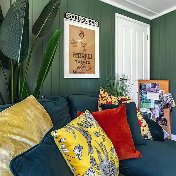 Interior of an insulated garden snug with dark green feature wall, tropical plant and plush velvet sofa