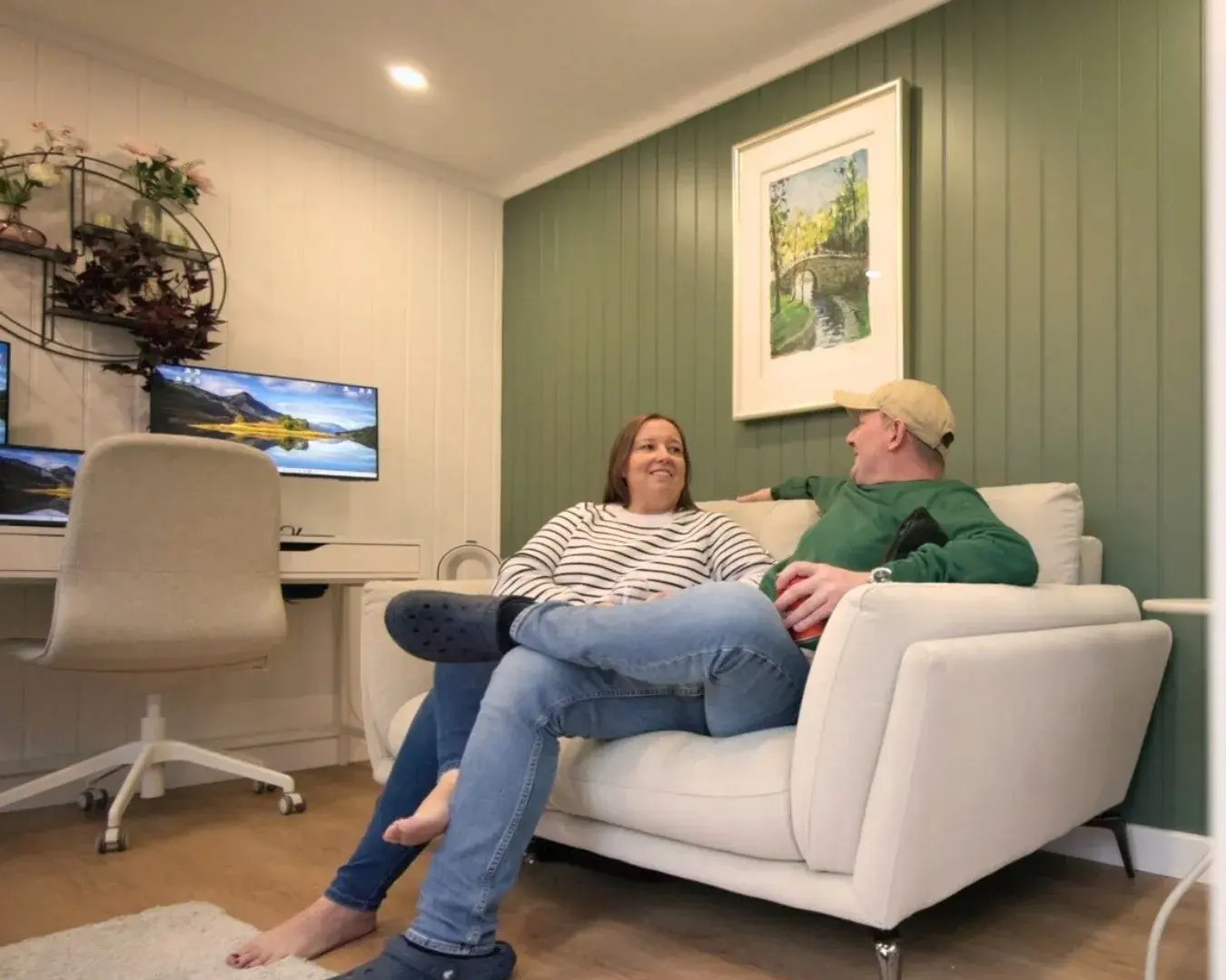 couple sat chatting on sofa inside a garden room with desk for homeworking