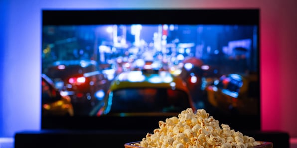 Image looking at a large screen TV with bowl of popcorn on table in front