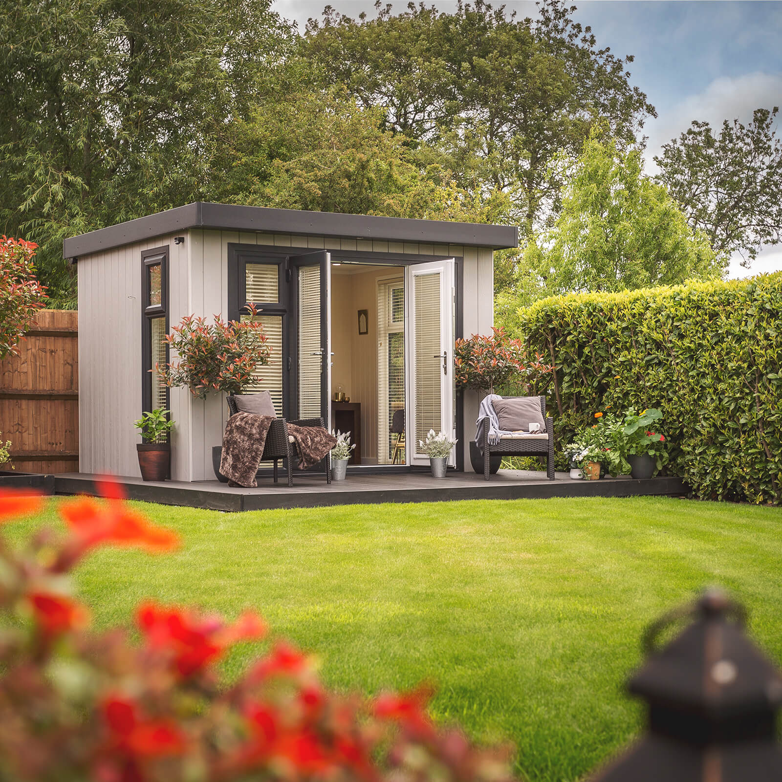 Small Summerhouse in large garden with timber step and garden furniture and potted plants