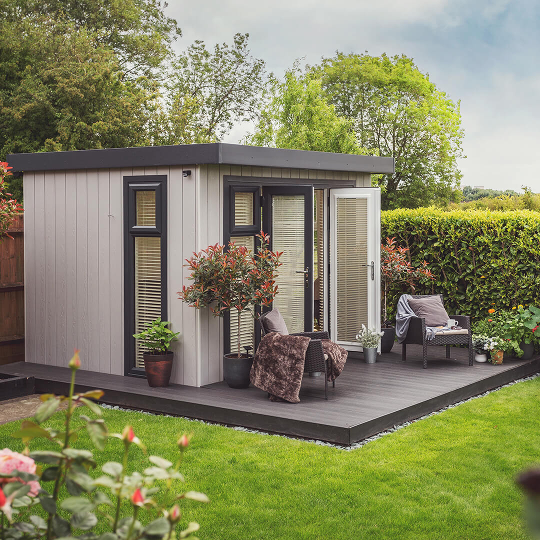 Cabin Master Cedar Summerhouse with large green lawn area and armchairs on timber decking