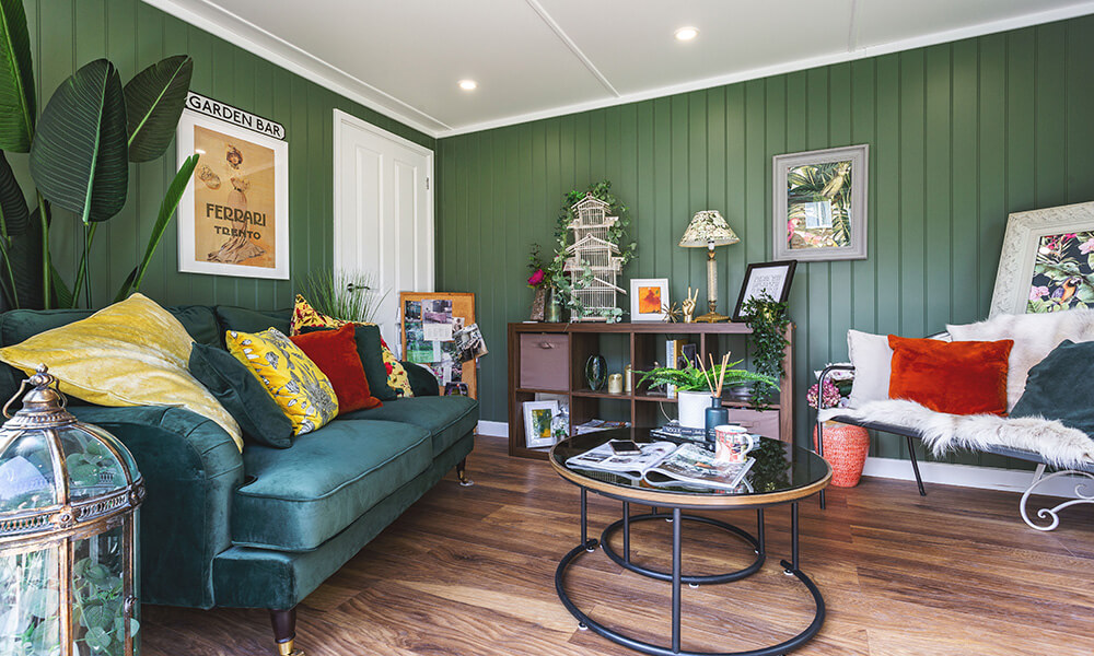 Interior of a cosy garden room snug with dark green walls and green velvet sofa