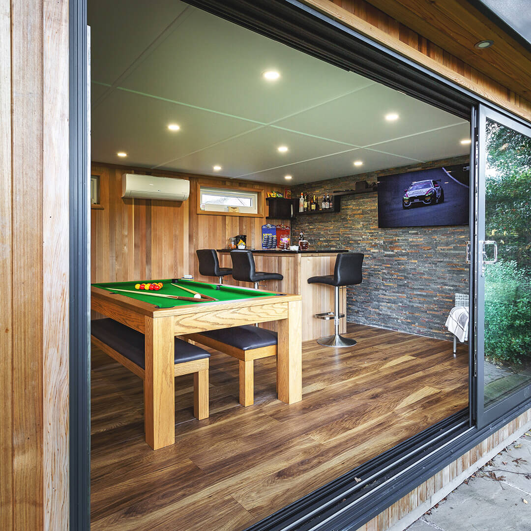 a timber man cave garden building with sliding glass doors and pool table and bar area inside