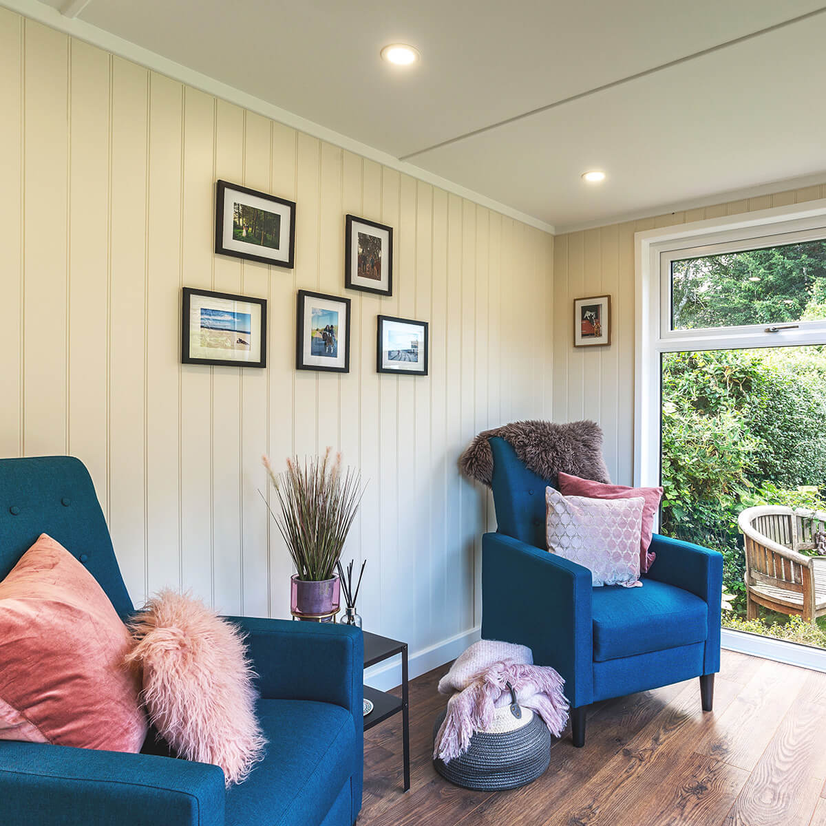 small garden room summerhouse with blue armchairs and framed pictures hanging on the wall