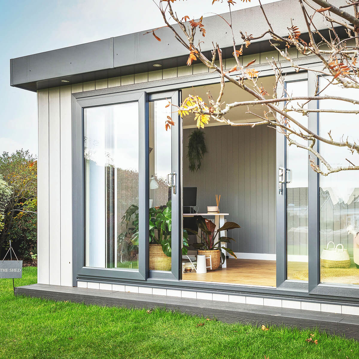 large garden office building with sliding glass doors and grassy lawn area with view of house plants and candle 