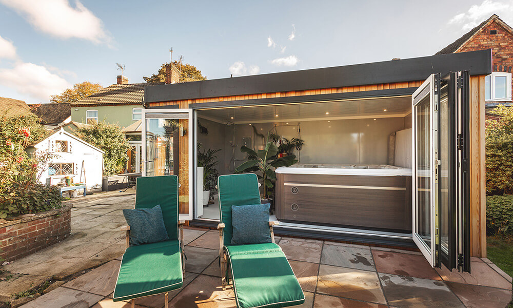 Hot tub garden room with open bifold doors and green sunloungers outside