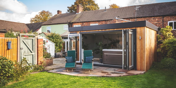 Garden spa room with hot tub inside with bifold doors open and bottle green sunloungers