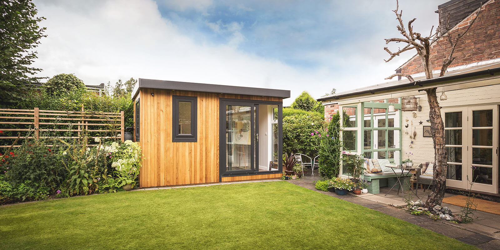 cedar garden room artists studio with green trellises and garden furniture and flowers and hedges