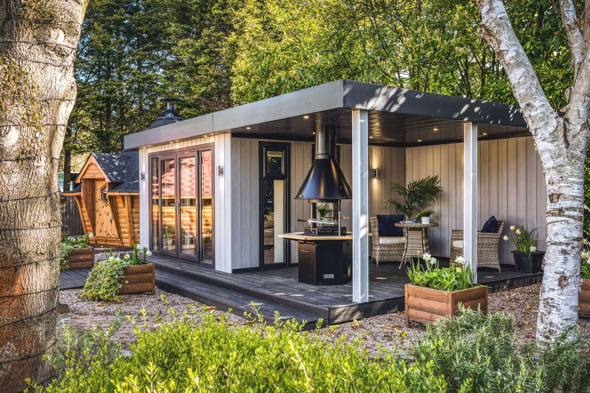 Show Site Grey Marley veranda room with BBQ Unit and composite decking with rattan furniture in background and potted plants in foreground