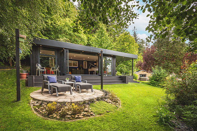 large marley board garden building with timber steps and garden furniture with patio area and large green lawn
