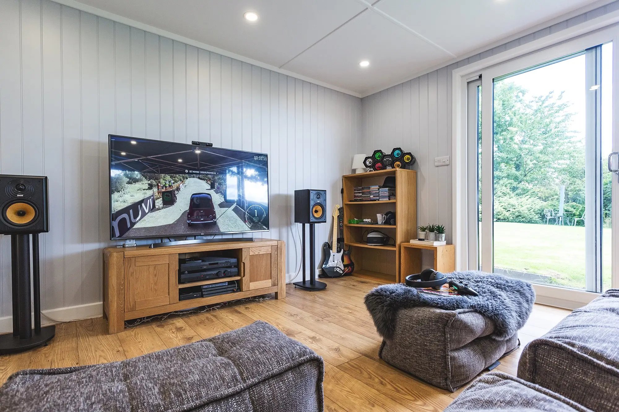 Inside view of garden room with grey sofas and foot stools and large flat screen TV with surround sound system and games console