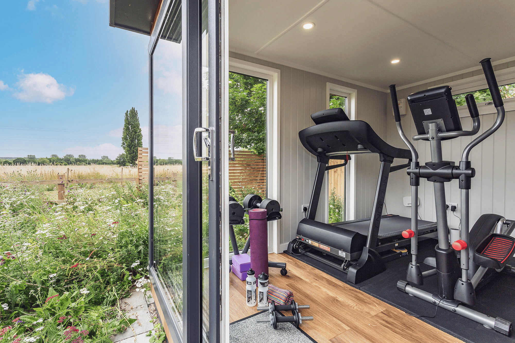 garden gym with sliding glass doors with laminate flooring and gym equipment and dumb bells and grassy outdoor area