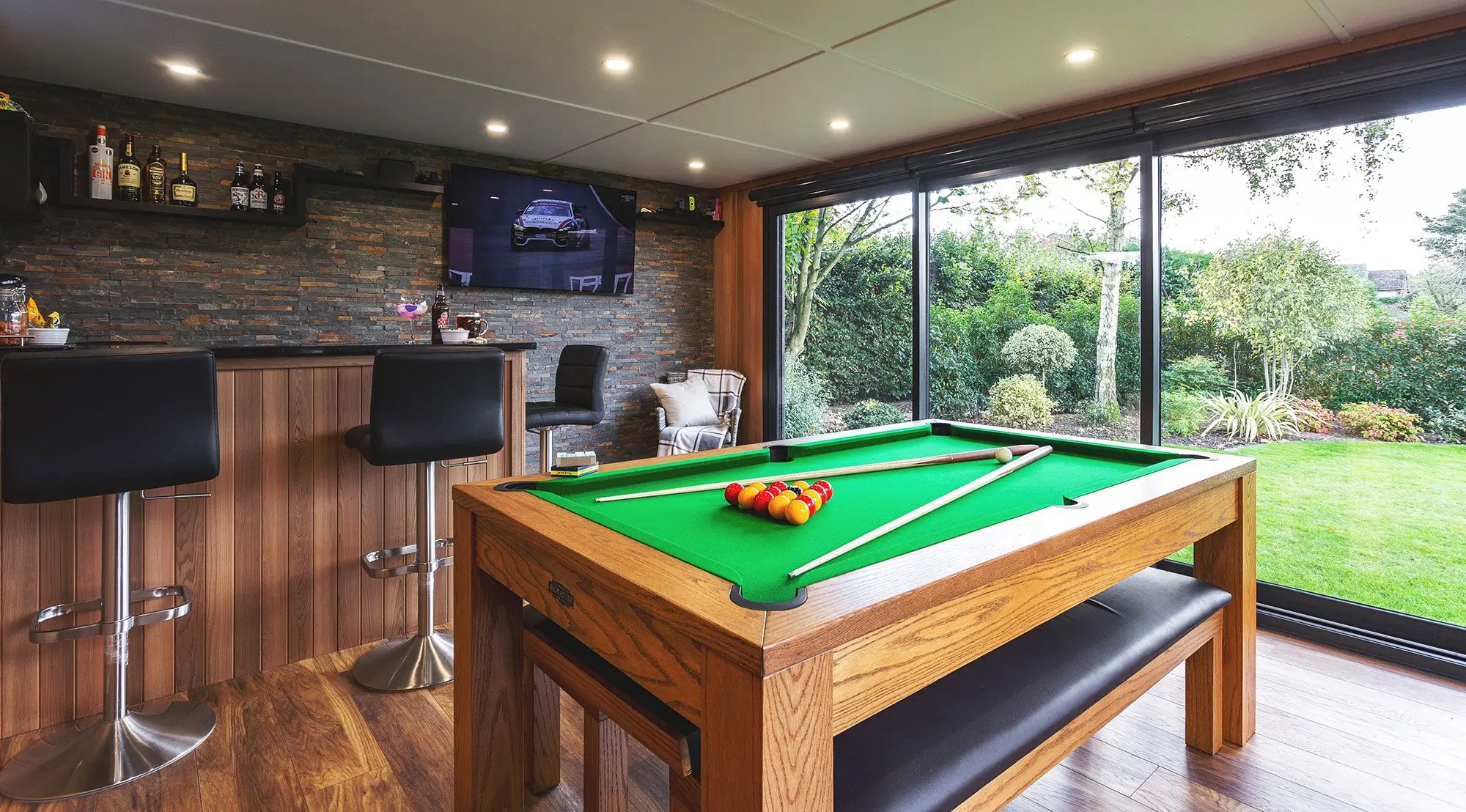 large garden bar with pool table and slate feature wall with flat screen tv hanging on it 