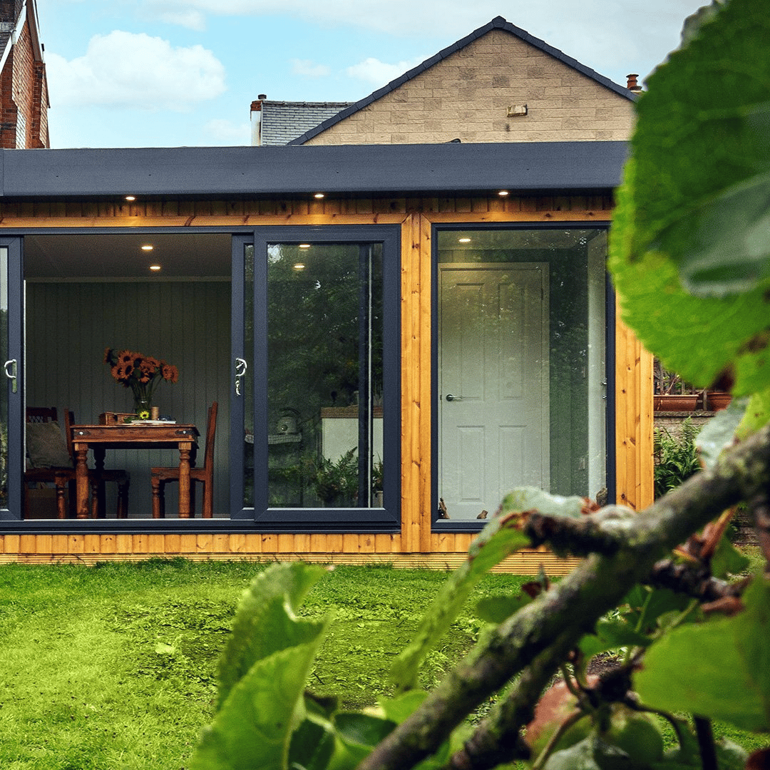 Large Redwood Garden Building in grassy lawn area with large glass sliding doors that are open