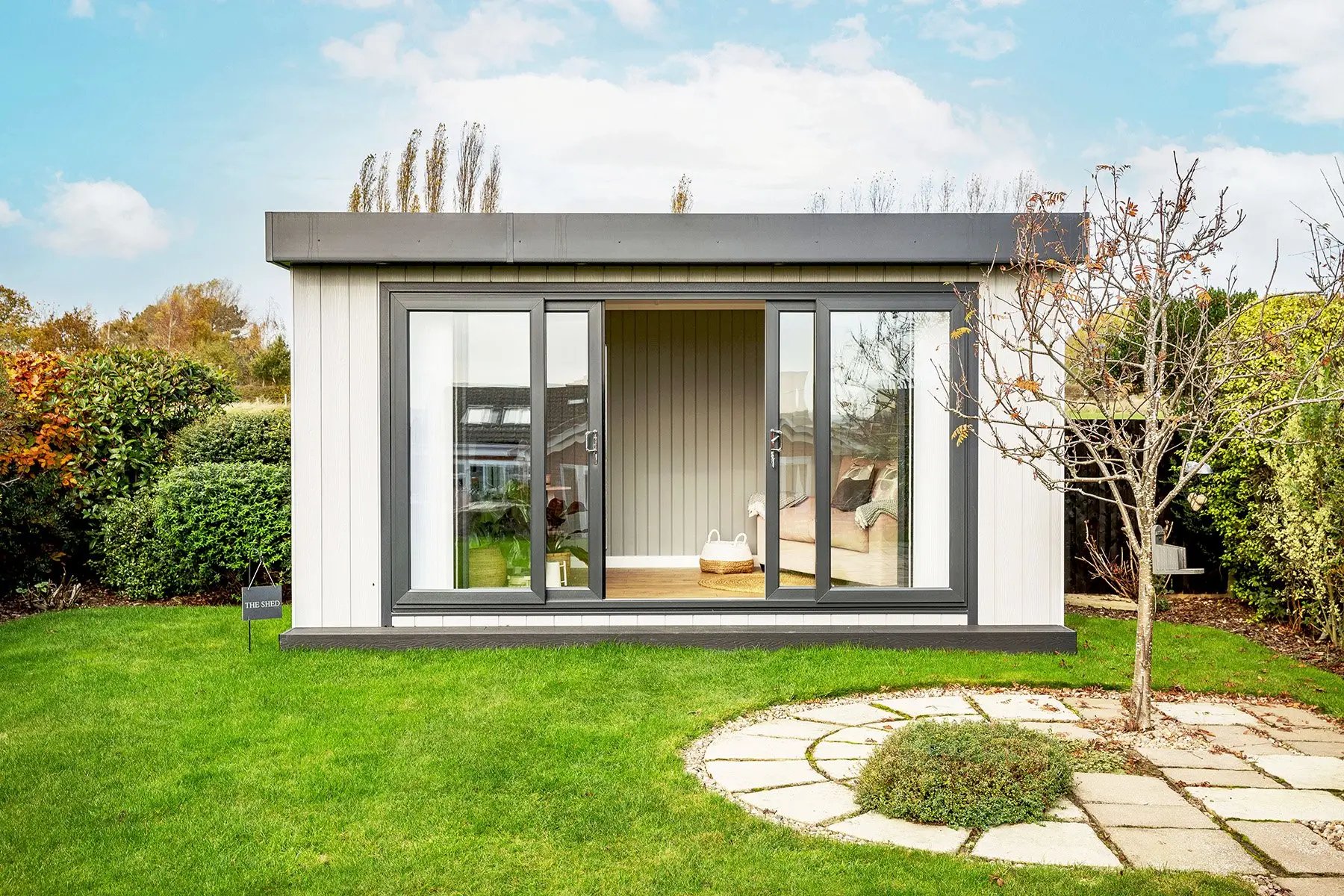 small garden office in grassy lawn area with sliding glass doors and small patio area