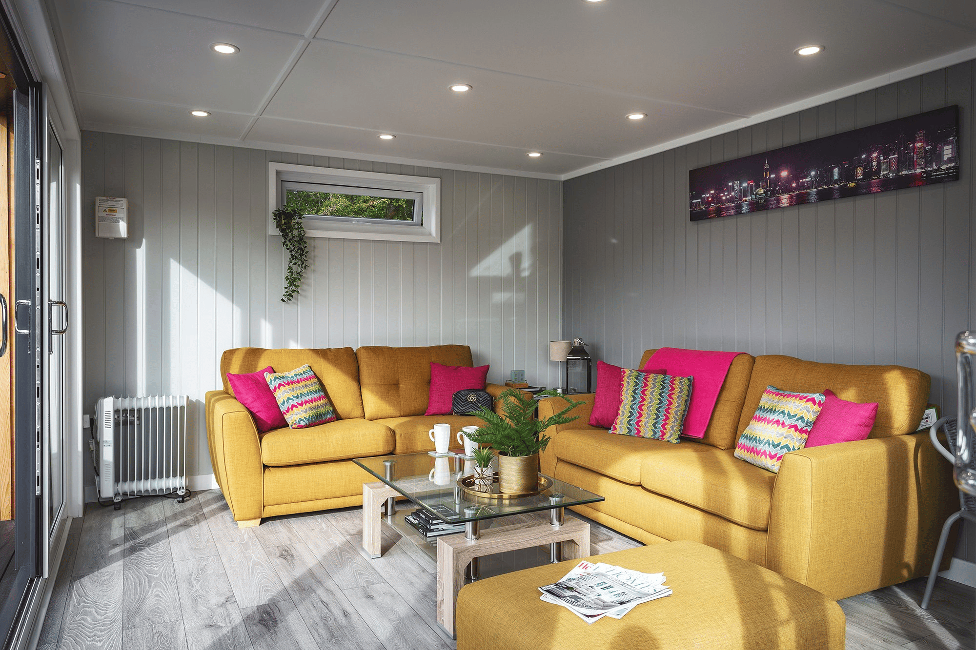 Inside of Garden Summerhouse with large yellow sofas and bright pink cushions with coffee table in the middle
