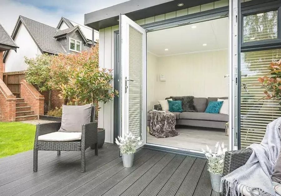 Contemporary garden room with open double doors leading onto grey composite decking with outdoor wicker chairs and a cosy indoor seating area.
