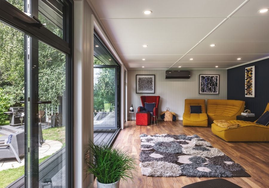 Spacious garden room lounge with mustard yellow sofas, a red armchair, wooden flooring and large bi-fold doors overlooking the garden.